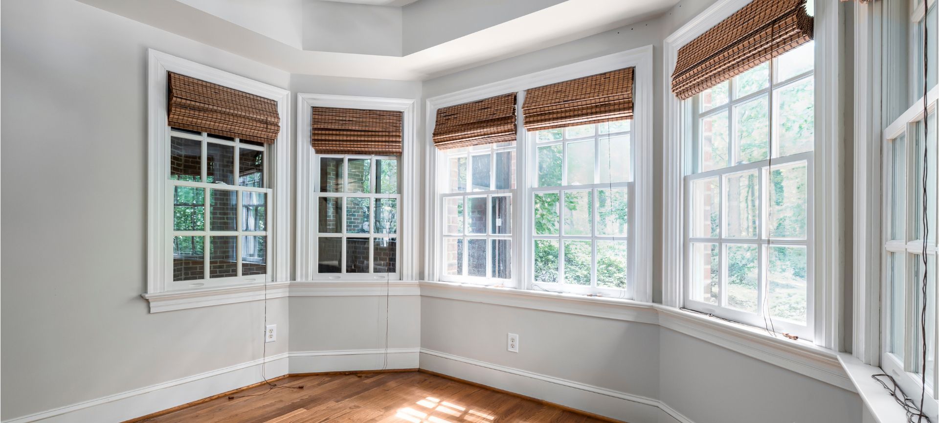 Empty bright bay window room with white walls, wood floors, and woven shades.