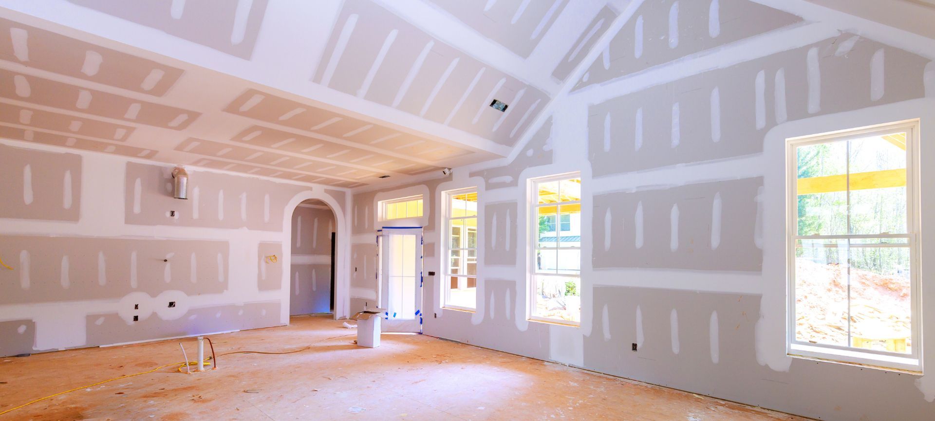 Empty drywall interior with unfinished walls, exposed floor, and sunlight through three windows.