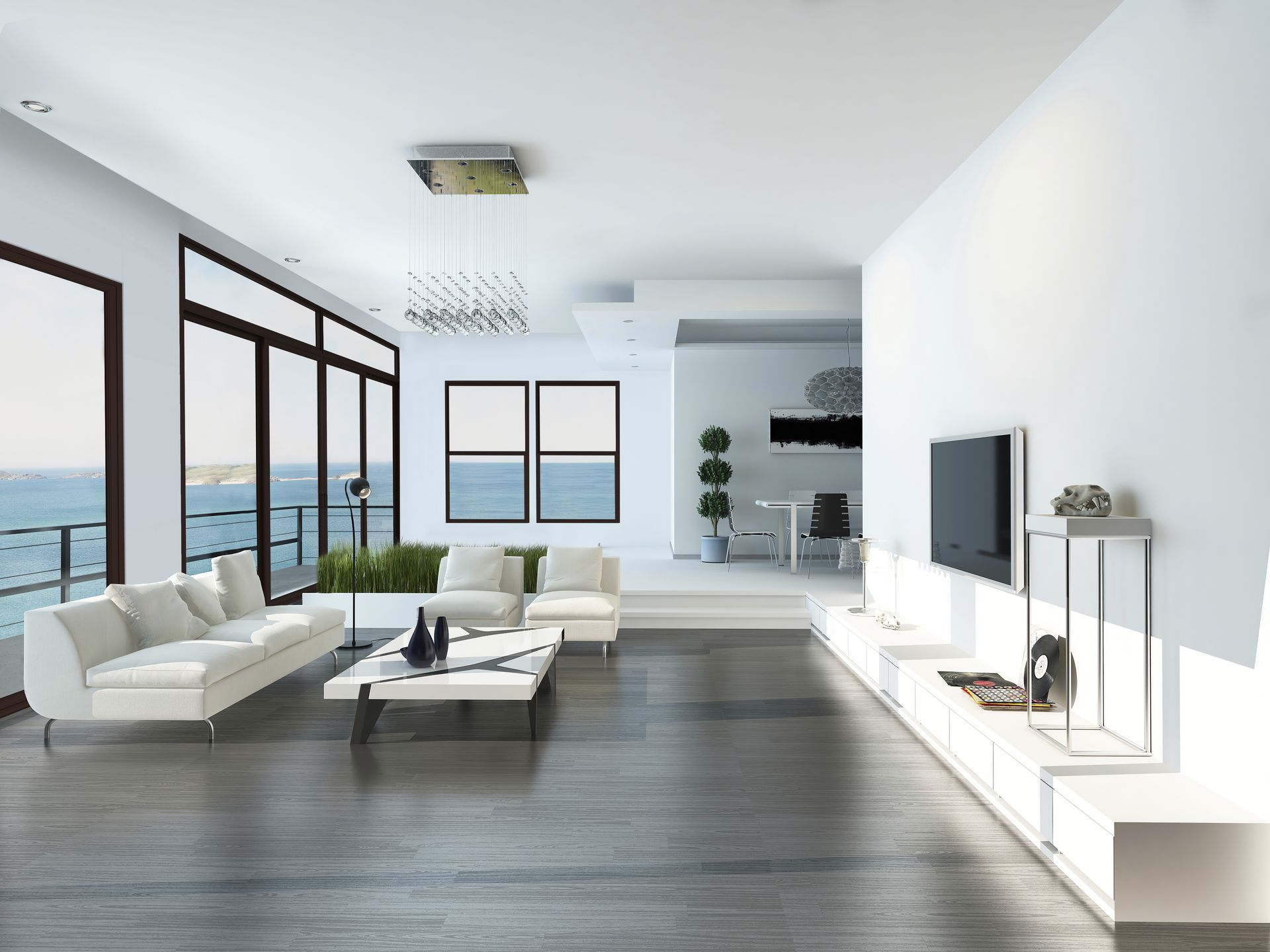 Modern living room with white furniture, large windows, ocean view, and a TV mounted on the wall.