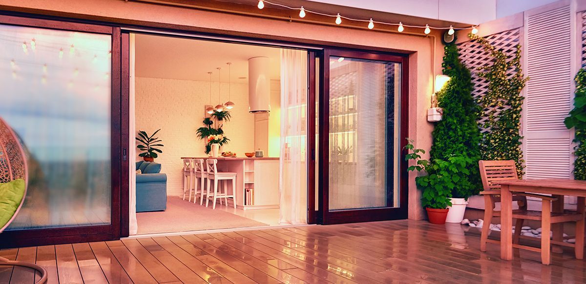 Modern patio with sliding glass doors, potted plants, and wooden bench seating at sunset.