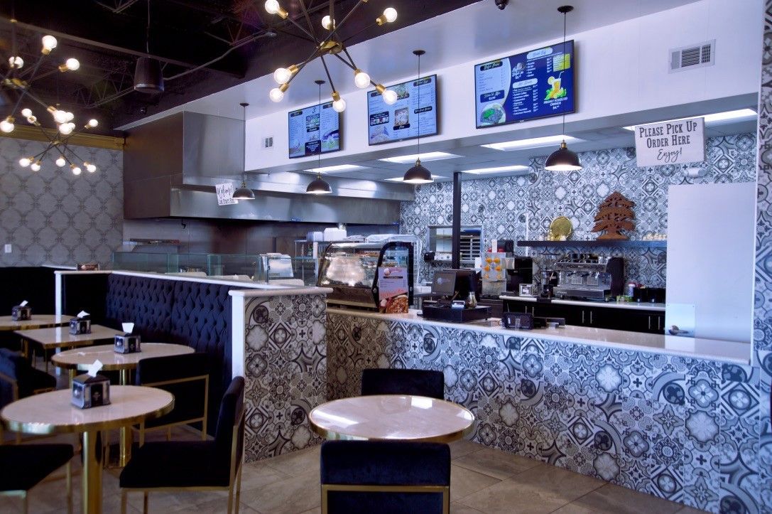 Interior view of a cafe with round tables, black chairs, and a patterned counter. Menu boards hang above the service area.