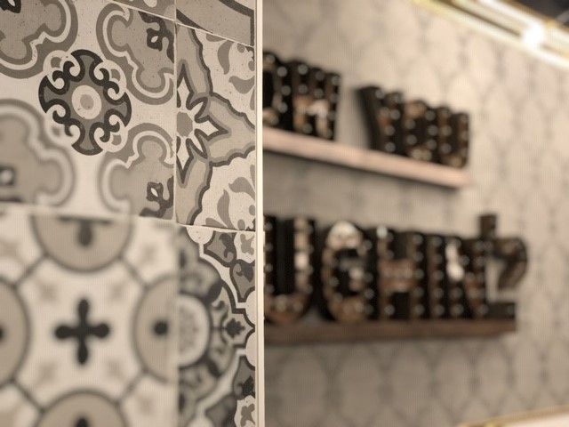 Decorative gray and white patterned tiles in the foreground, with a blurred wall and shelf displaying