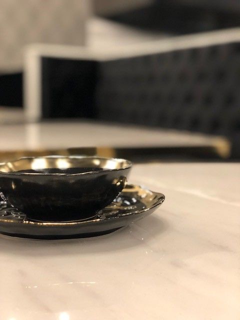 Black teacup and saucer with gold trim on a white marble surface.