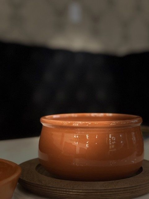 Orange ceramic bowl on a wooden coaster, blurred dark background.