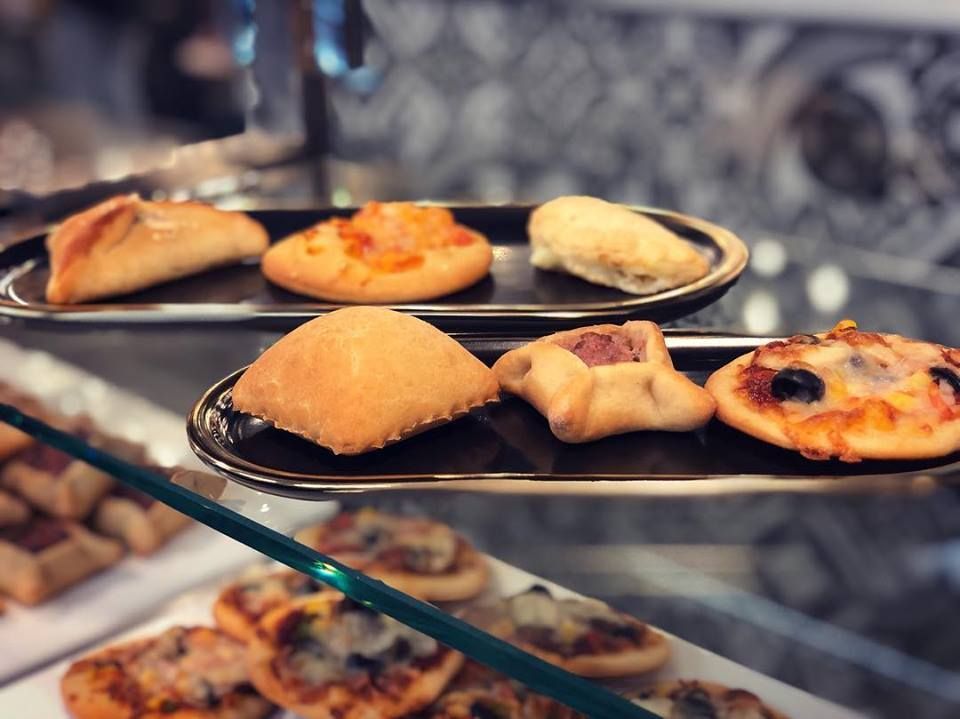 Pastries on display in a bakery case, including small pies and pizza-like baked goods.