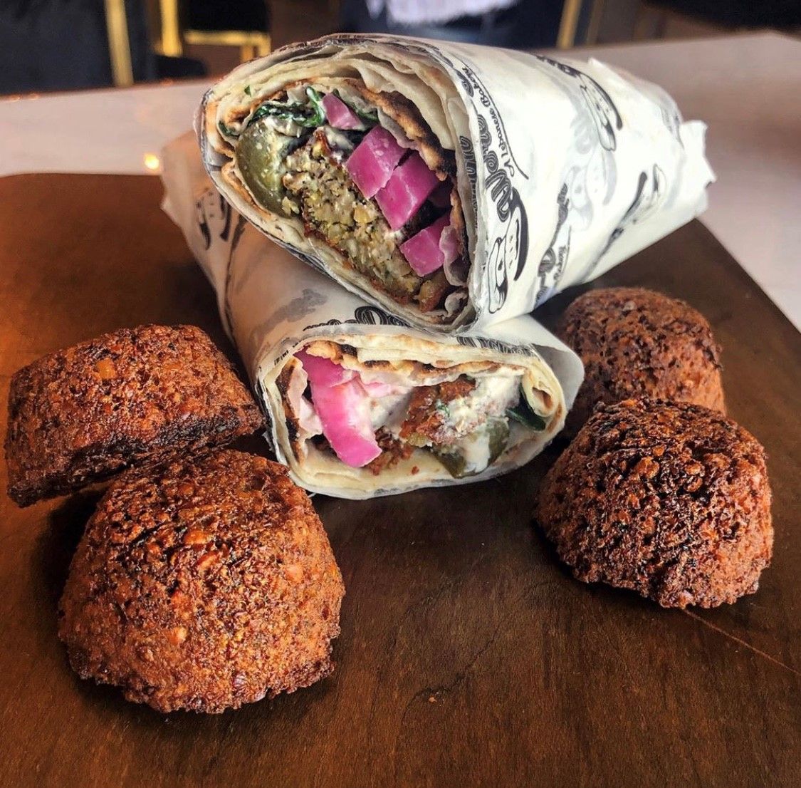 Falafel wrap cut open, with falafel balls on wooden board. Pickled onions and sauce visible.