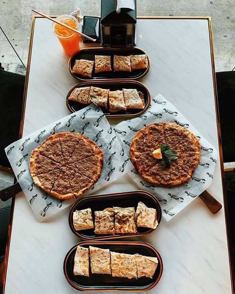 Overhead shot of Middle Eastern food spread on a white marble table: flatbreads, filled pastries, and drinks.