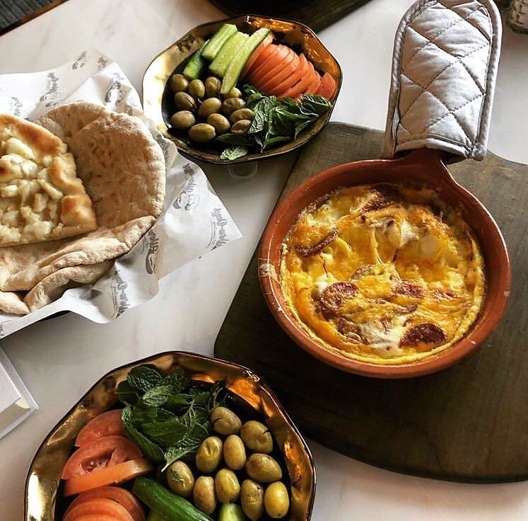 Overhead shot of a meal with bread, olives, vegetables, and a baked dish in a handled pot.