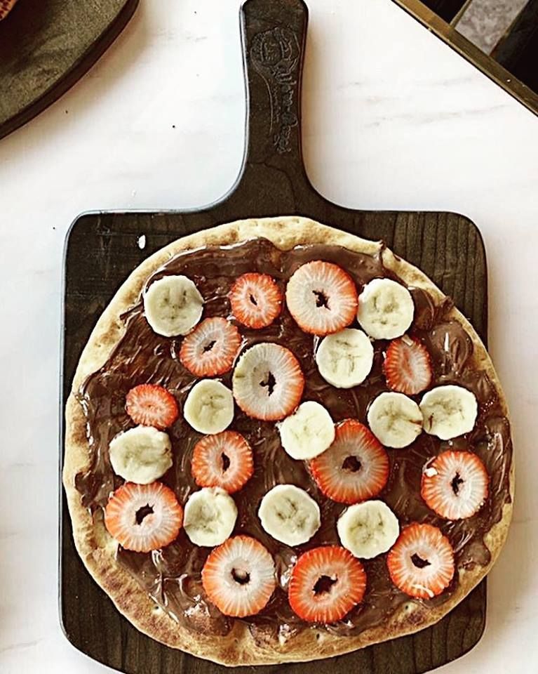 Nutella fruit pizza: dough topped with Nutella, strawberries, and banana slices on a wooden board.