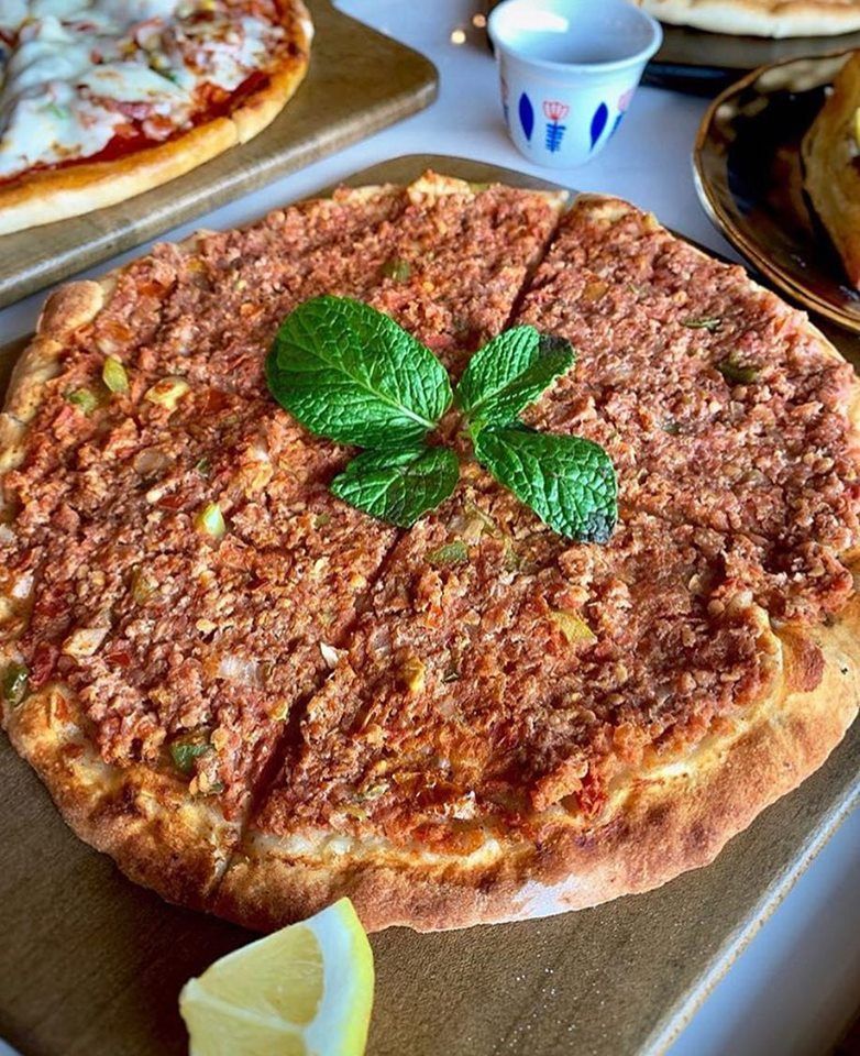 Lahmacun, a thin flatbread topped with minced meat and vegetables, garnished with mint and lemon.