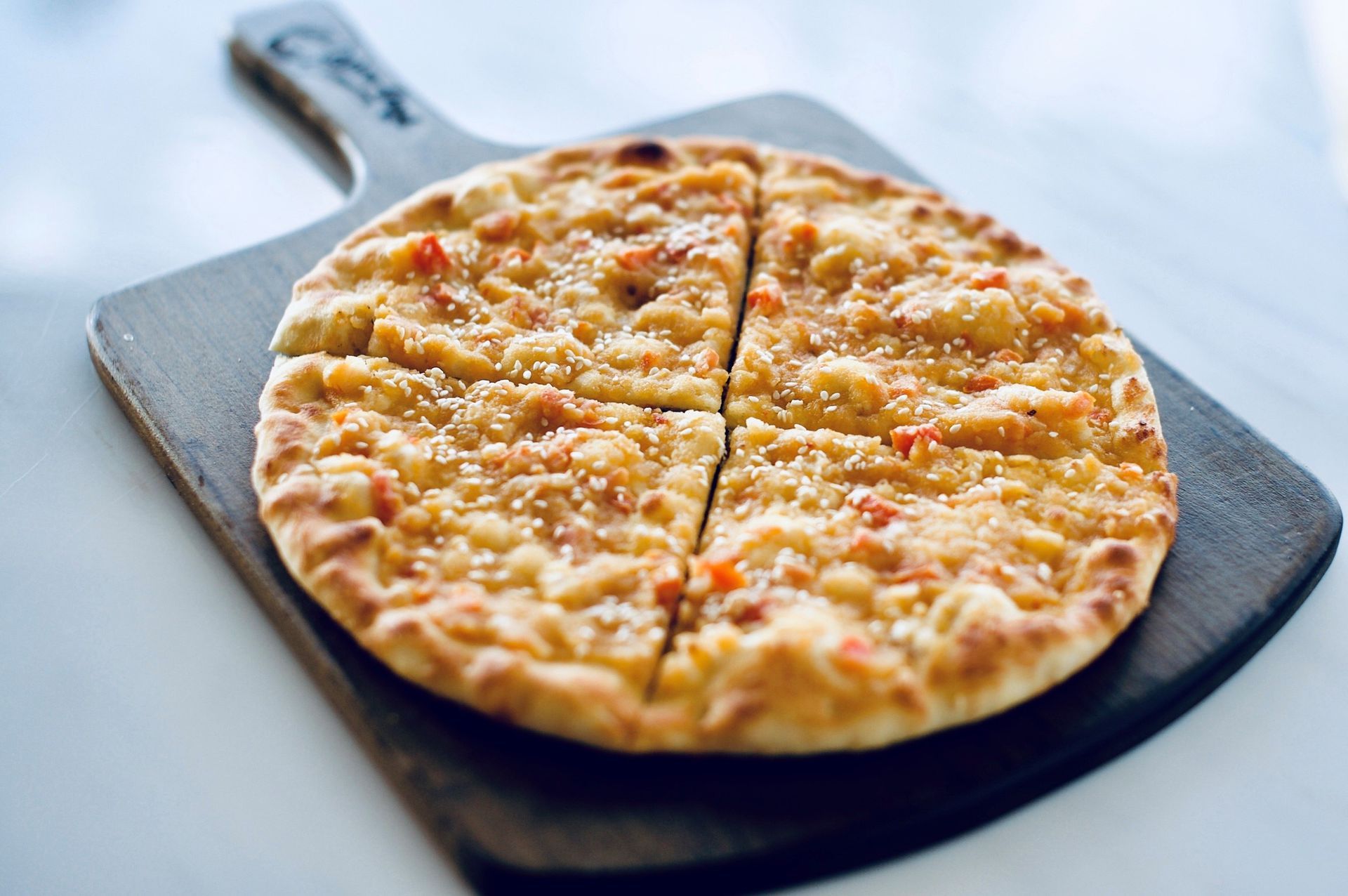 Pizza on a wooden board, cut into four slices, topped with cheese and sesame seeds.