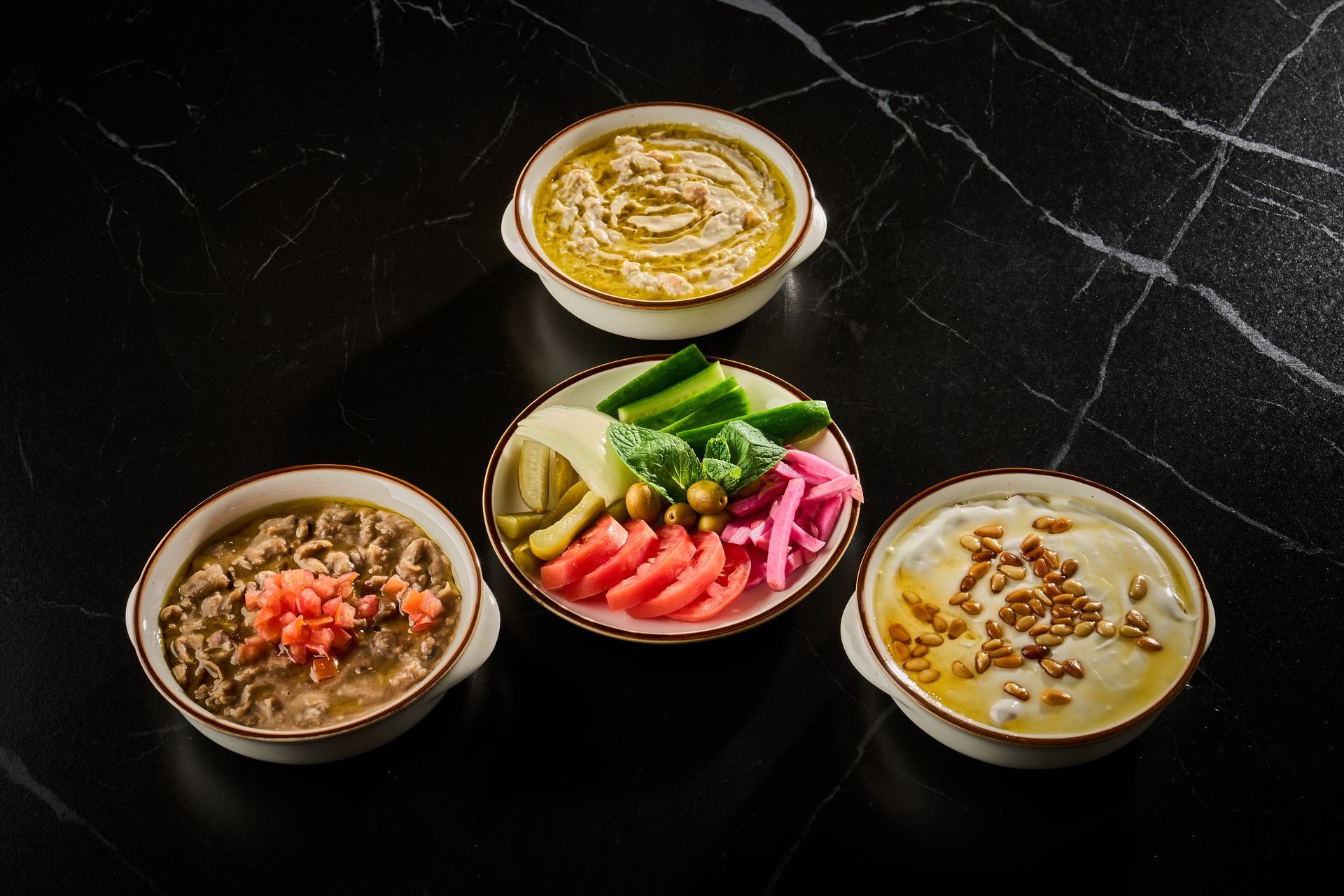 Three dips with garnish on a dark background. One dip is green, one is tan with red, and one is tan with pine nuts.