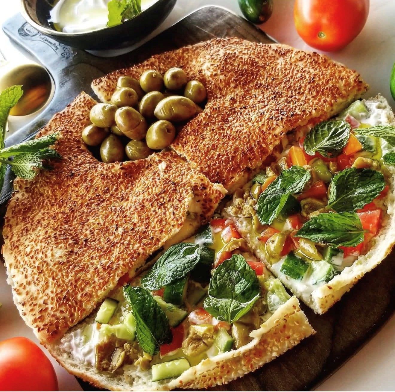 Flatbread platter with olives, fresh vegetables, and mint garnish.
