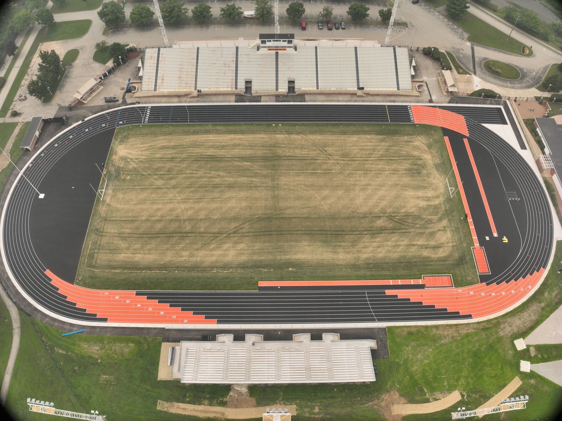 Aerial view of an empty outdoor stadium with a grassy field, running track, and bleachers.