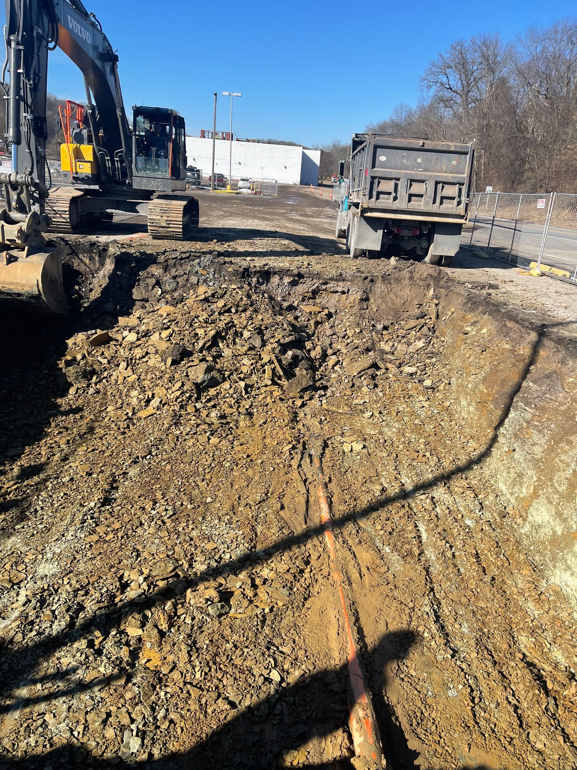 An excavator is digging a hole in the dirt next to a dump truck.