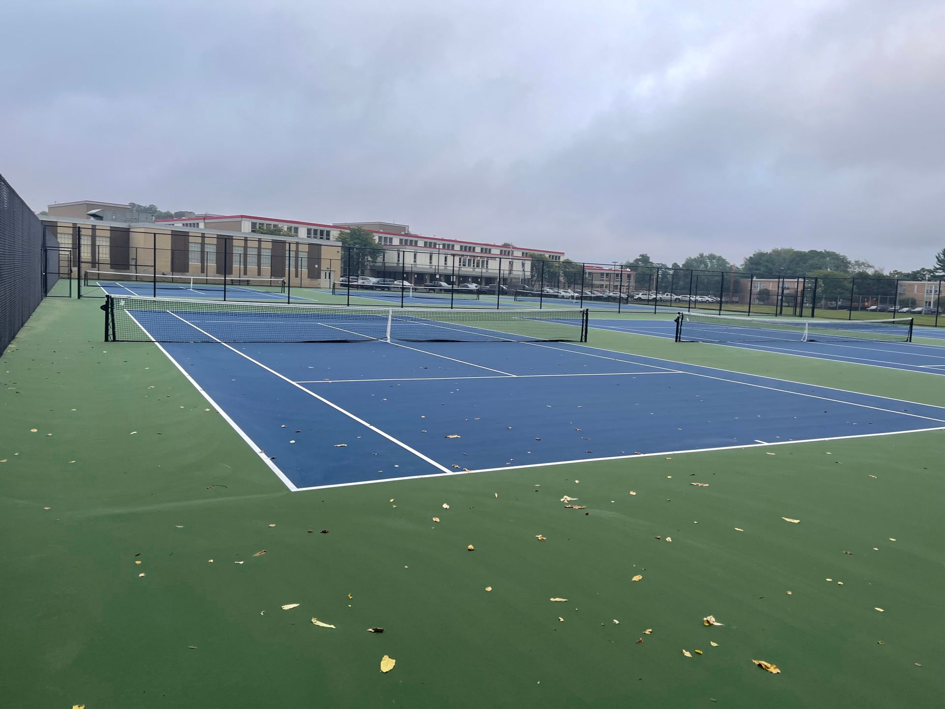 A tennis court with buildings in the background on a cloudy day