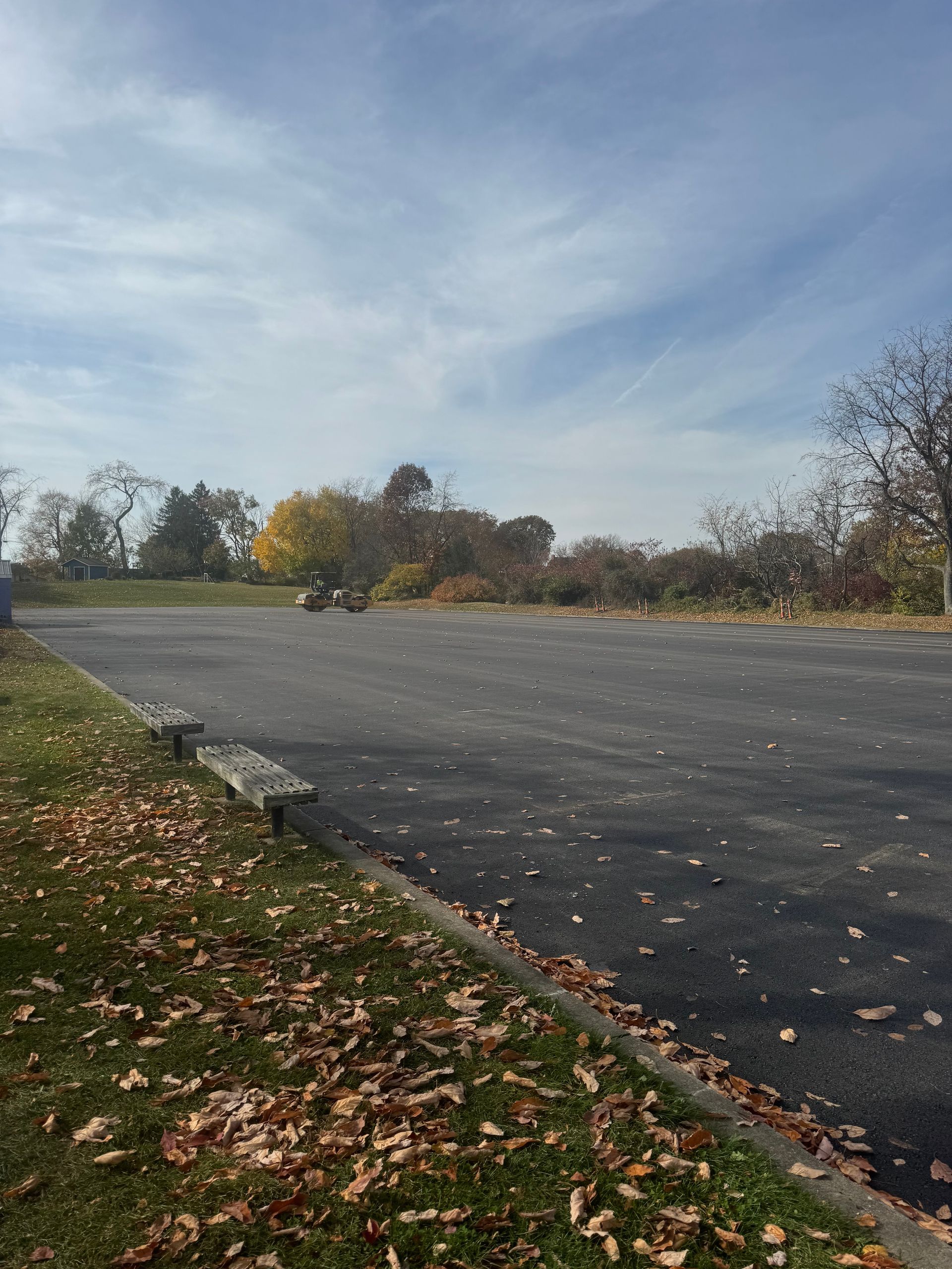 A parking lot with a bench and leaves on the ground on a sunny day.