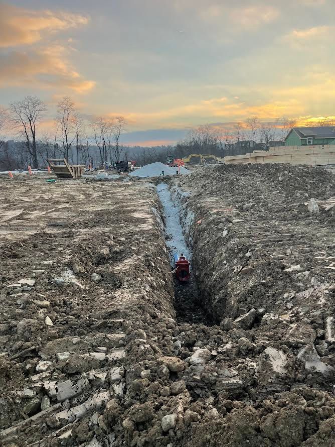 A man is standing in a trench in the middle of a dirt field.