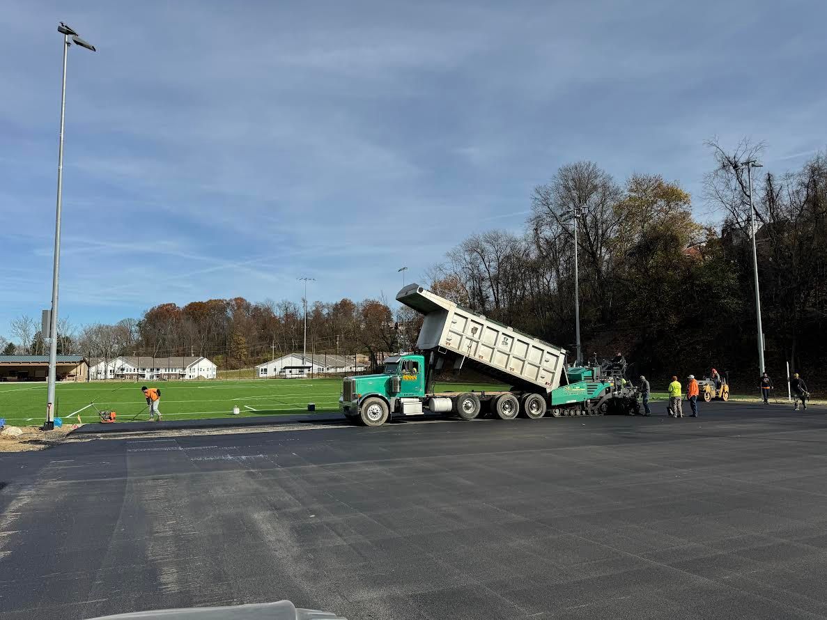 A dump truck is sitting in a parking lot next to a field.