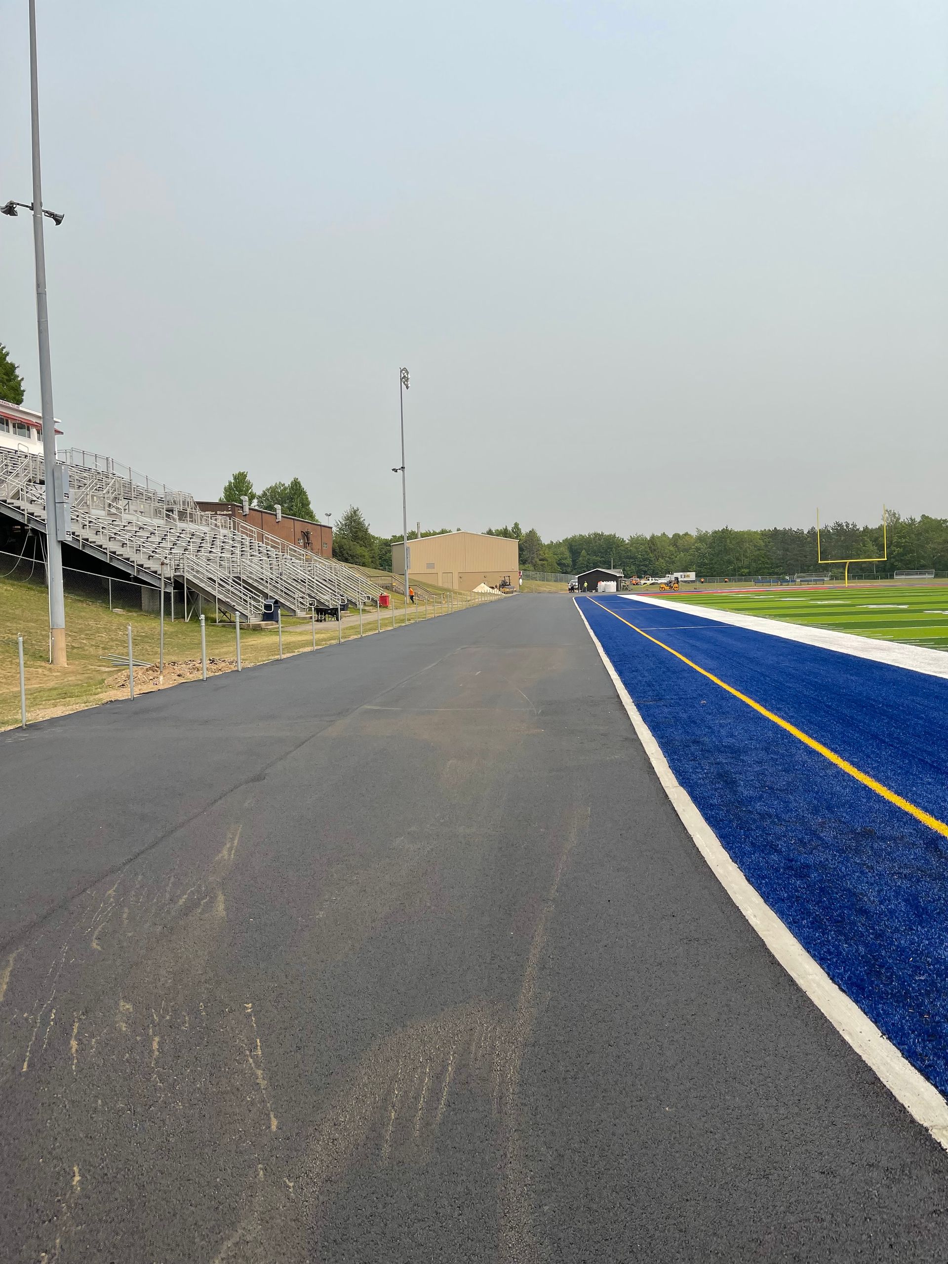 A road leading to a stadium with blue grass and bleachers.
