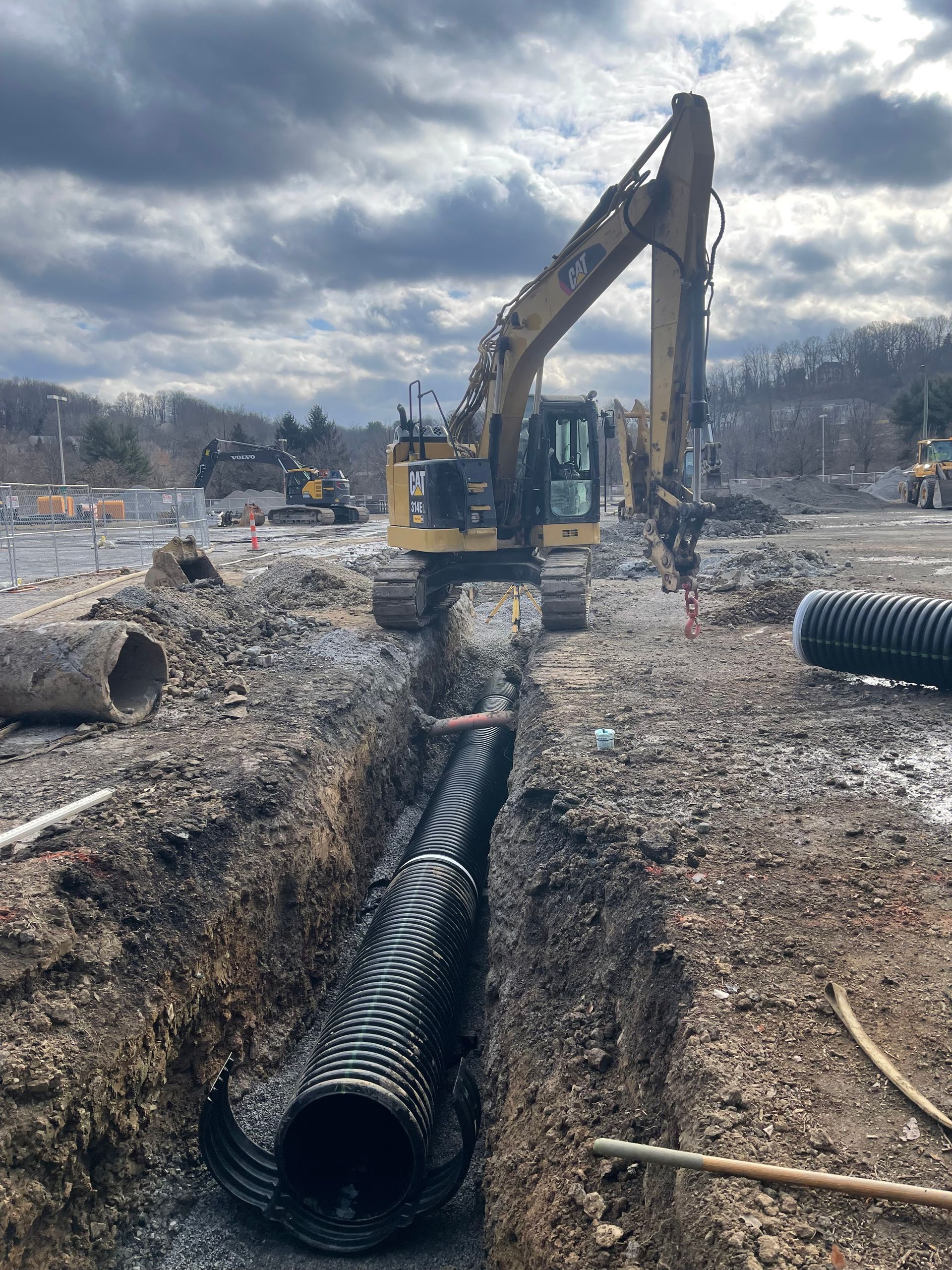 A large excavator is digging a hole in the ground next to a large pipe.