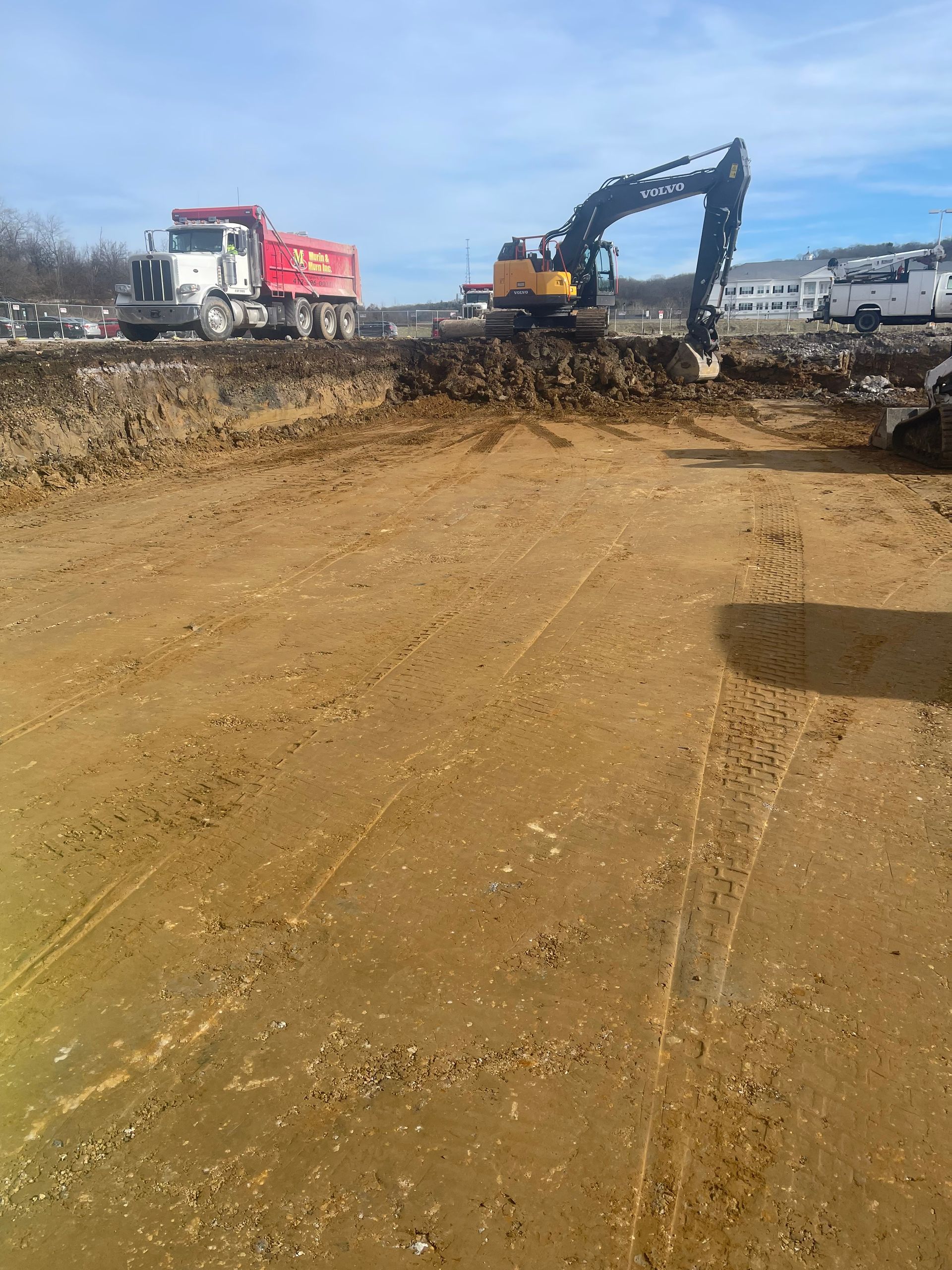 A large excavator is digging in a dirt field next to a dump truck.