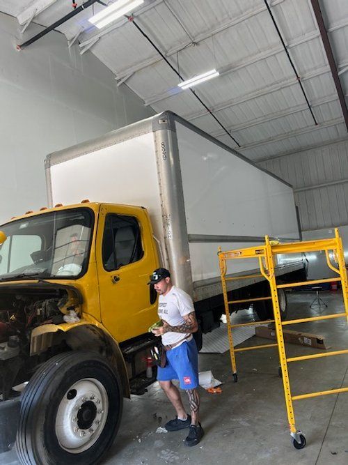 A man is working on a yellow truck in a garage.