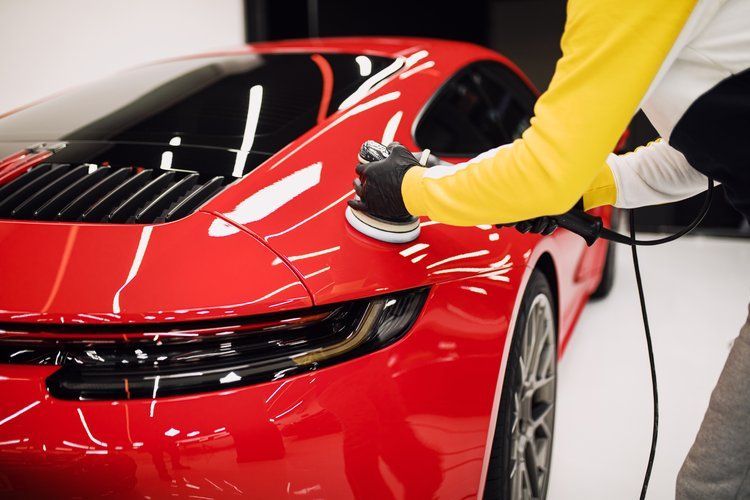 A man is polishing a red sports car with a machine.