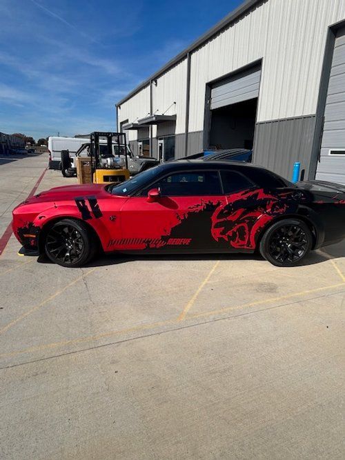 A red dodge challenger is parked in front of a building