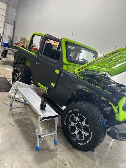 A green jeep is parked in a garage with the hood up.