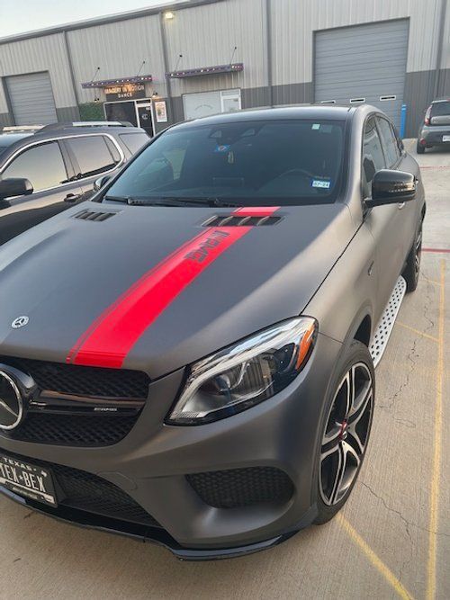 A black car with a red stripe on the hood is parked in a parking lot.