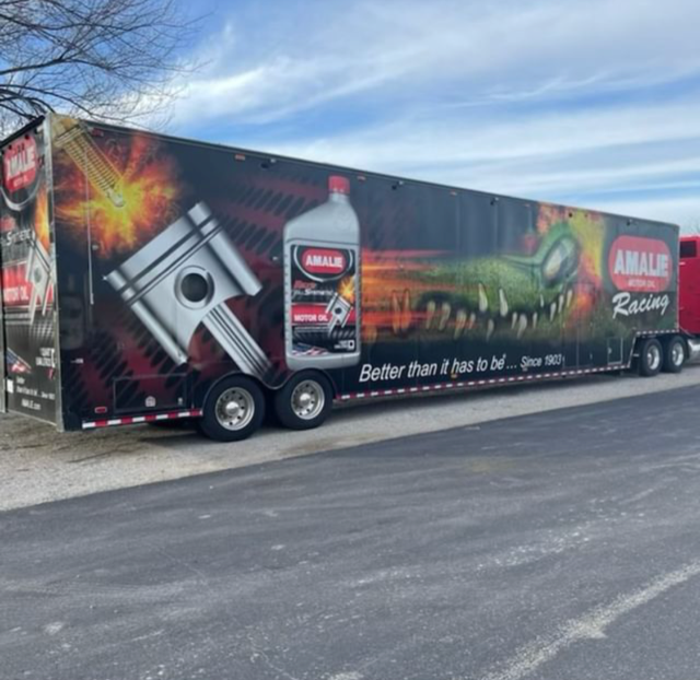 A large amalie racing trailer is parked on the side of the road