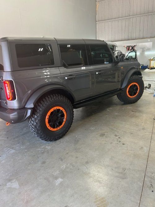A gray ford bronco with orange wheels is parked in a garage.
