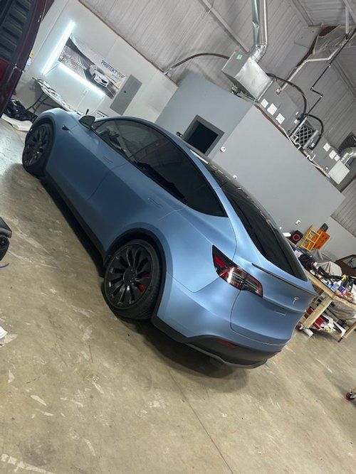 A blue tesla model 3 is parked in a garage.