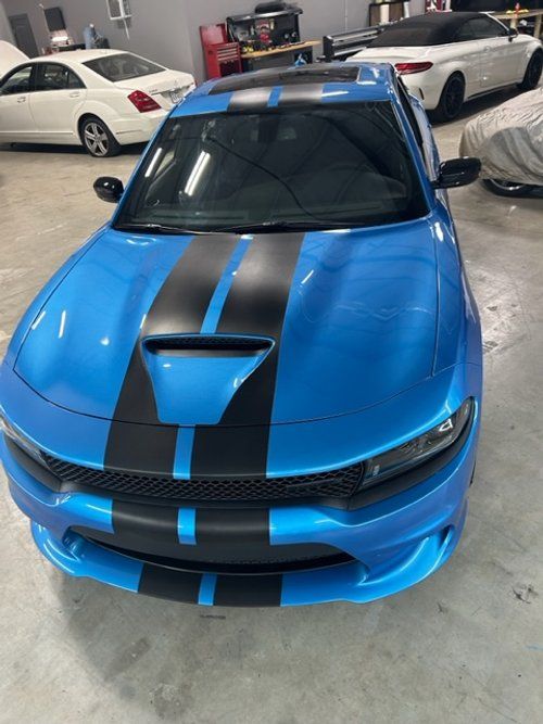 A blue dodge charger with black stripes is parked in a garage.