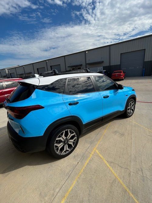 A blue and white car is parked in a parking lot in front of a building.
