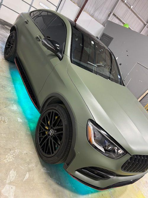 A green car with blue lights underneath it is parked in a garage.