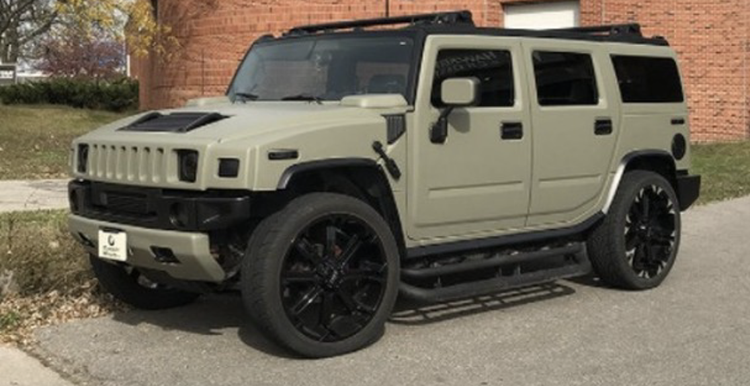 A hummer h2 is parked on the side of the road in front of a brick building.