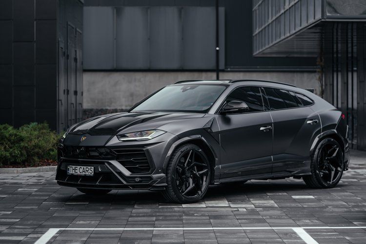 A black lamborghini urus is parked in a parking lot in front of a building.