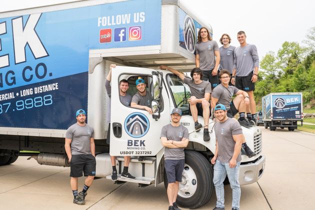 BEK Moving Co. team posing with white moving truck and box truck outside warehouse