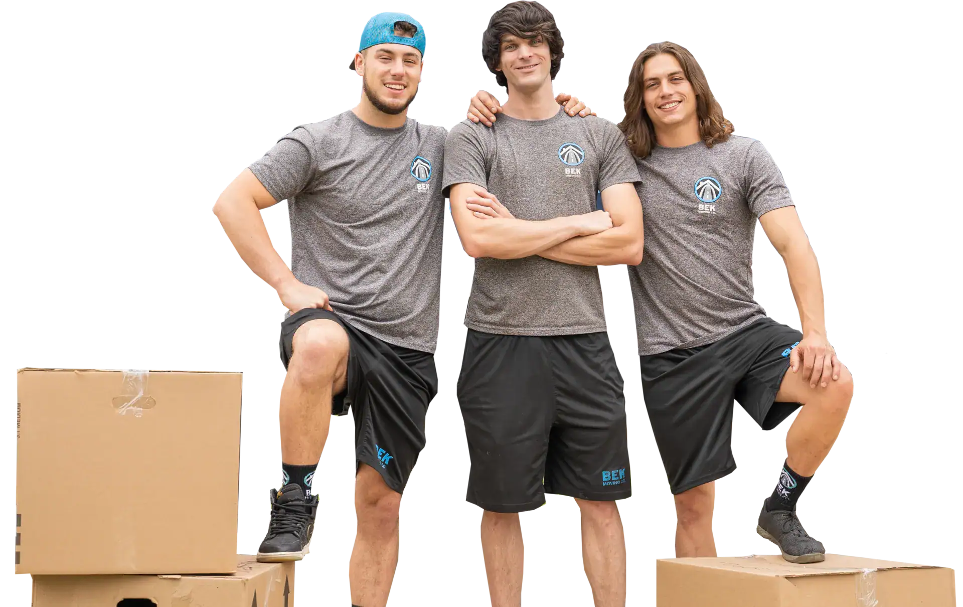 Three movers in gray shirts standing on cardboard boxes, posing with crossed arms and raised knees.