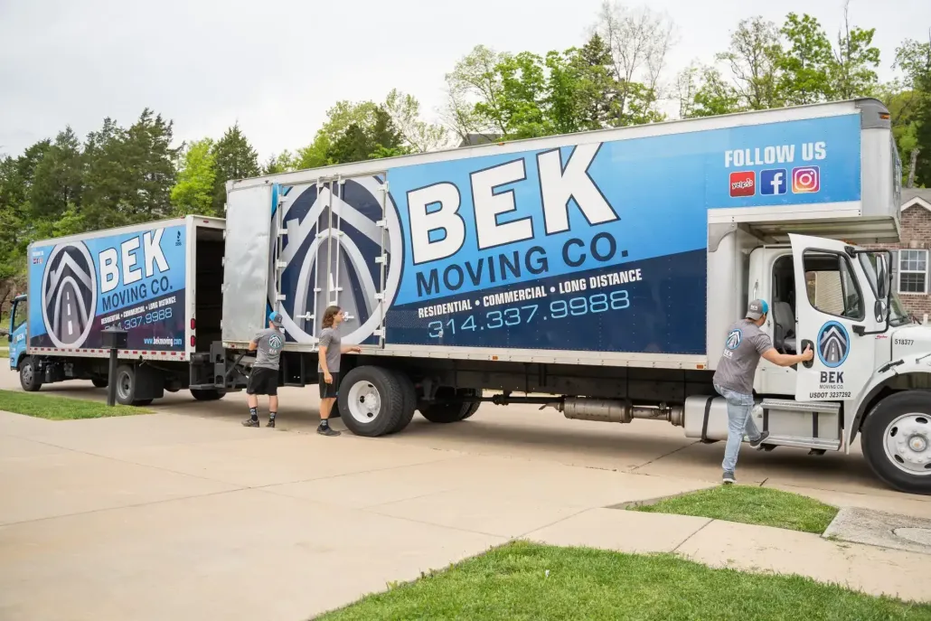 BEK Moving Co. trucks with blue logos parked outside a building, workers loading in daylight