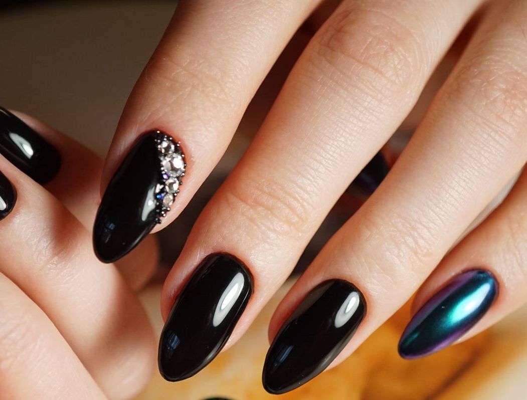 A close up of a woman 's nails with black nail polish and rhinestones
