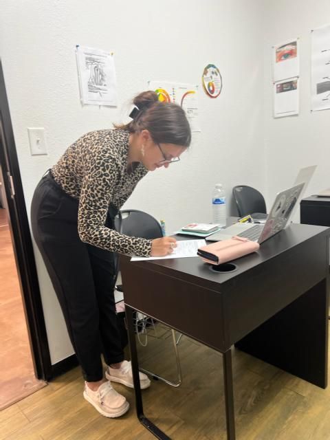 A woman is standing at a desk writing on a piece of paper.