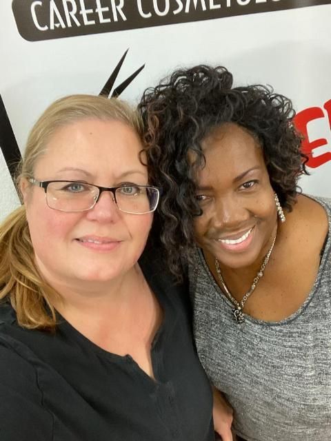 Two women are posing for a picture in front of a sign that says career cosmetics