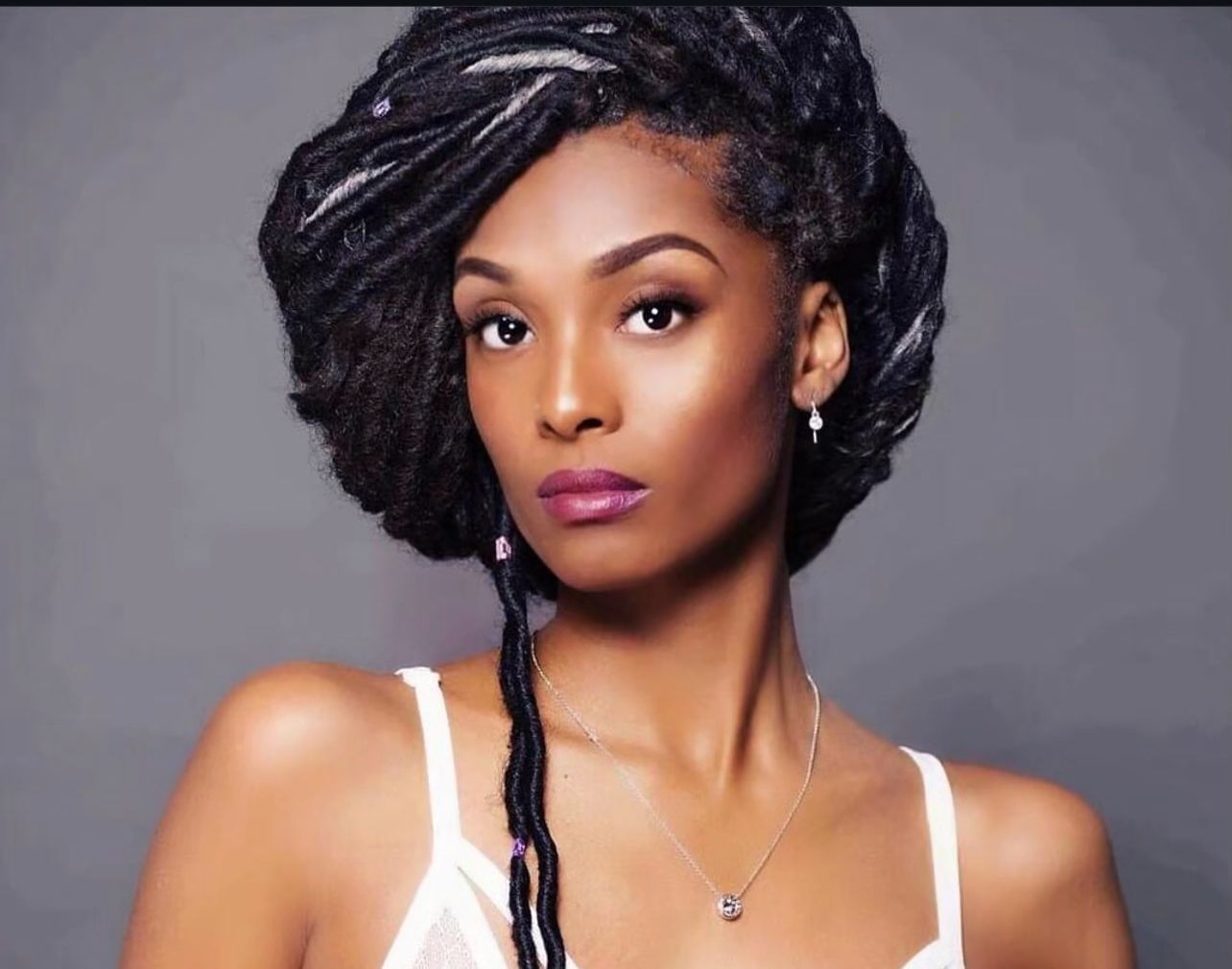 A woman with dreadlocks is wearing a white tank top