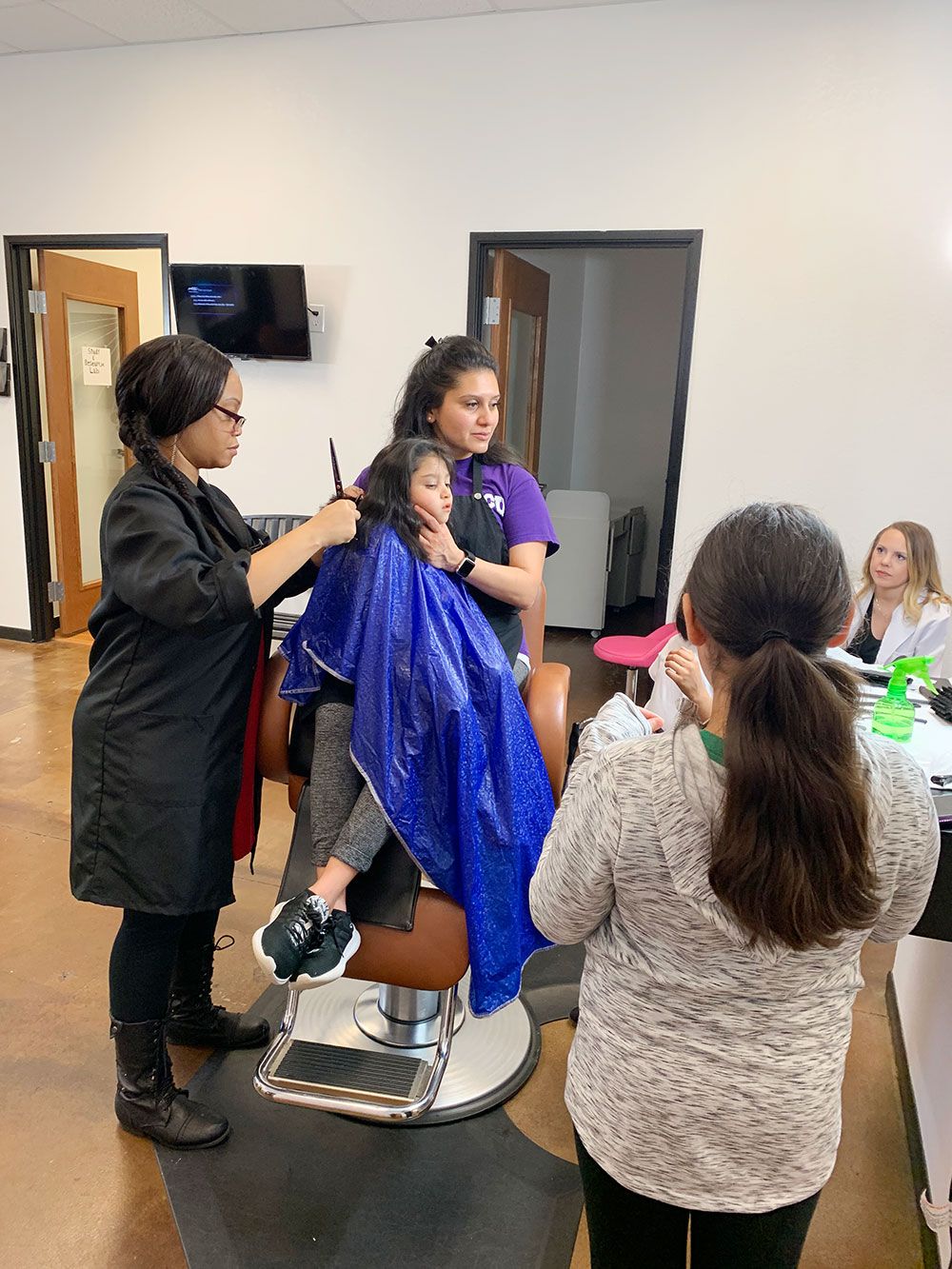 A woman is cutting a little girl 's hair in a barber shop.