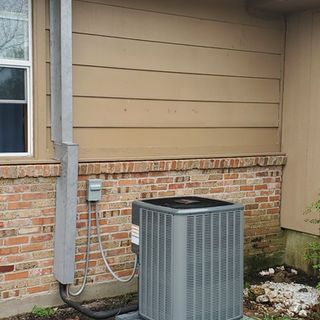 An air conditioner is sitting on the side of a brick house.