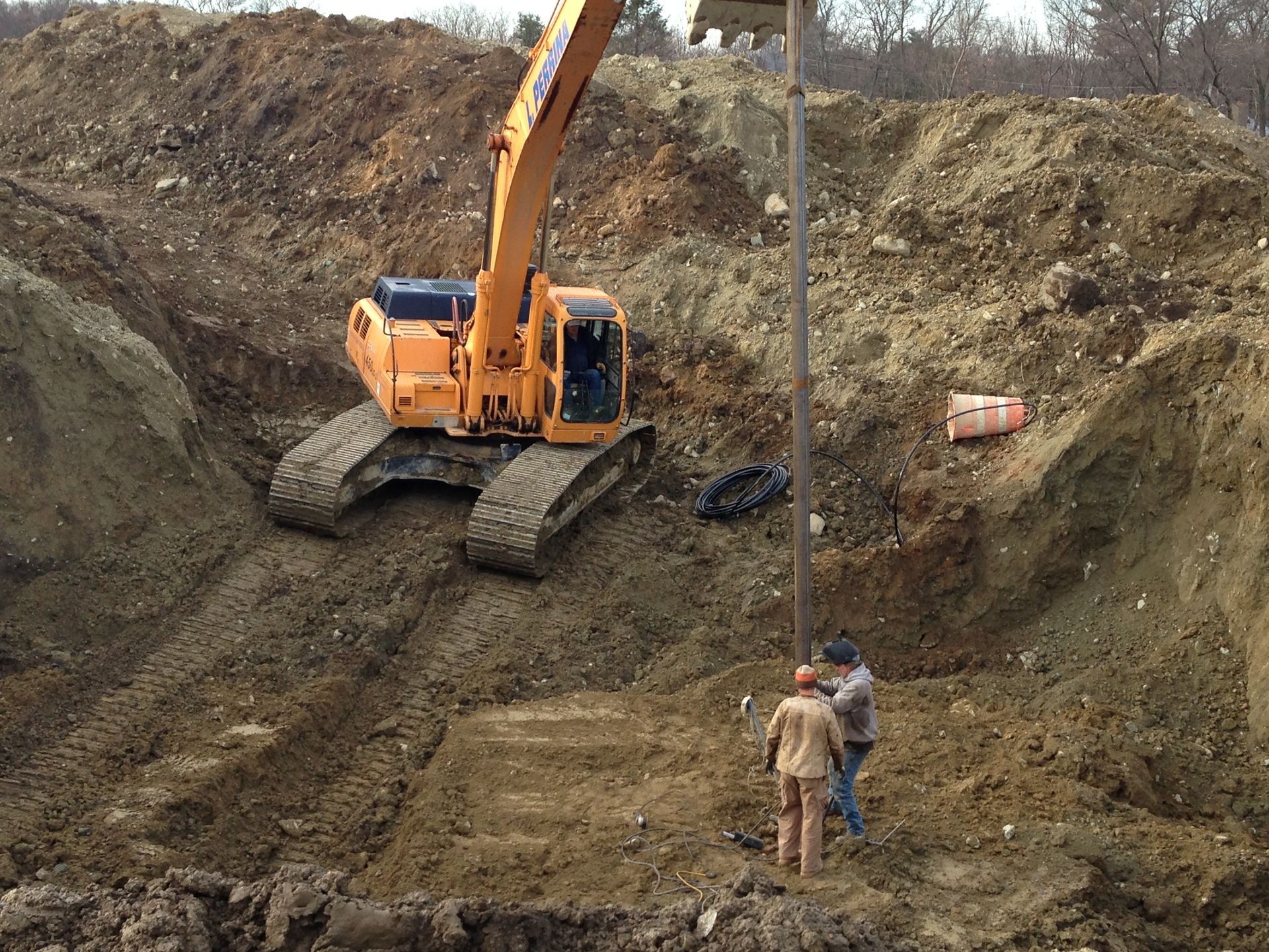 Excavator and workers in a deep dirt trench at a construction site