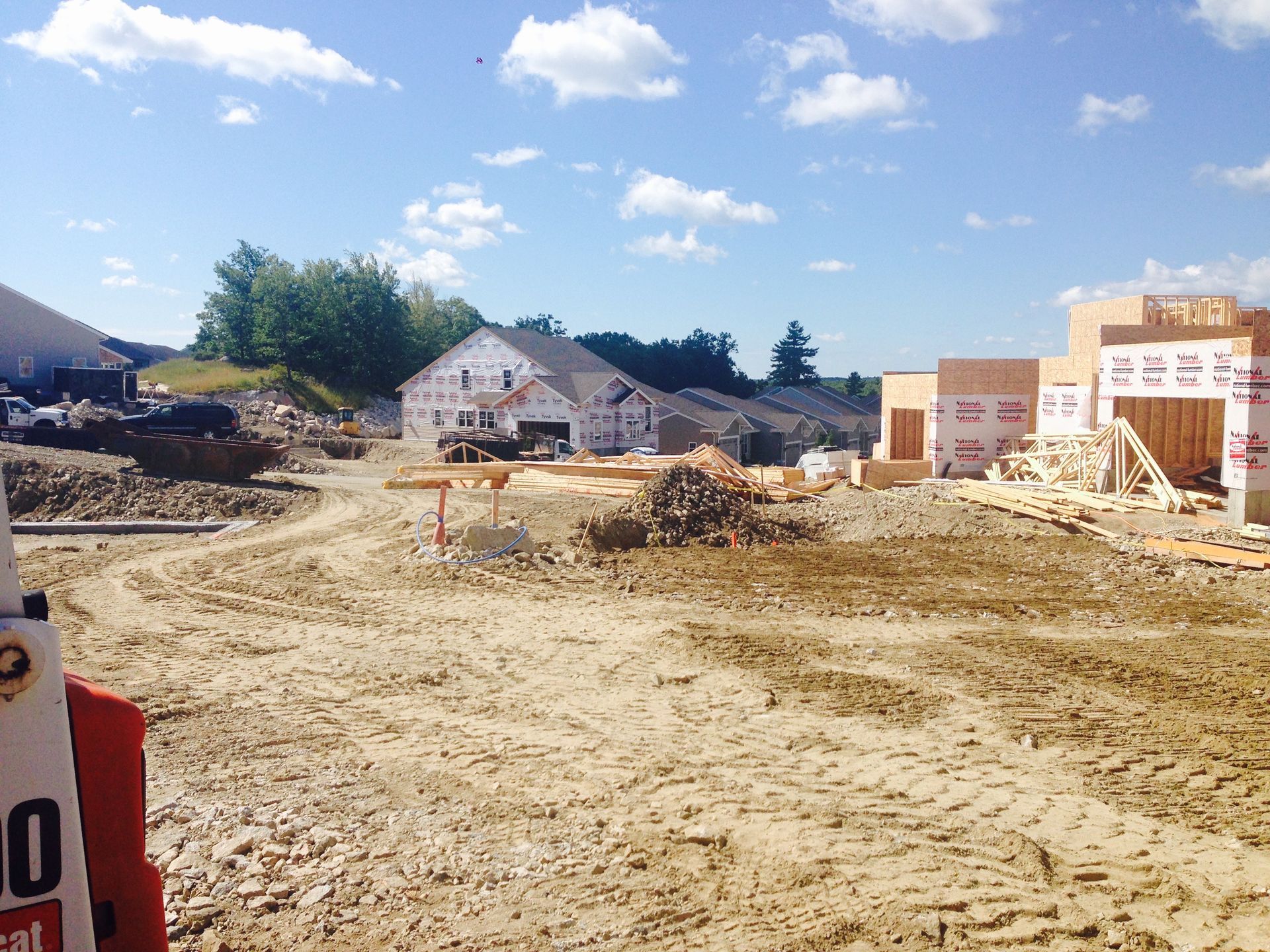 Construction site with dirt lot, unfinished buildings, and construction materials under a blue sky